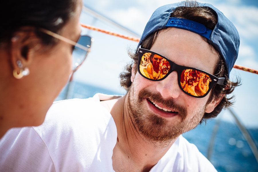Lachender Mann mit Kappe und Sonnenbrille auf einem Segelboot